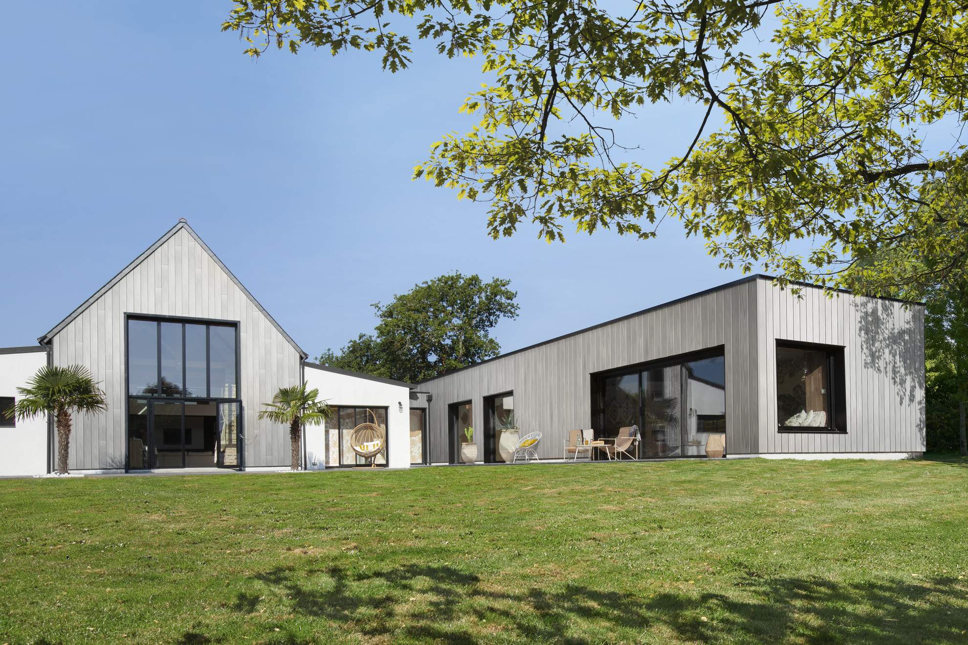 Moderne woning met gevelbekleding van Silvadec composiet hout, bestaande uit twee aparte volumes met zadeldak en plat dak, omgeven door een groene tuin
