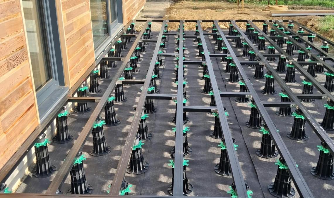 Ossature de terrasse en lambourdes aluminium Réversil sur plots, le long de la façade d'une maison
