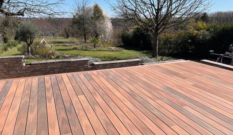 Terrasse en bois composite Silvadec installée dans un jardin de campagne avec muret en pierre et vue sur un verger, aménagement paysager par Agave Paysage