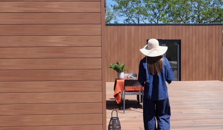 Jonge vrouw met hoed loopt naar een tafel en Bardage Atmosphère 175 Brun Soleil Silvadec